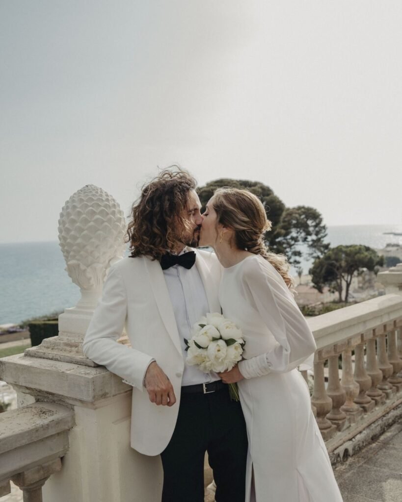 Gemma y su pareja frente al mar en Santa Romana, vestido de novia de crepé con chaqueta de gasa de puños drapeados