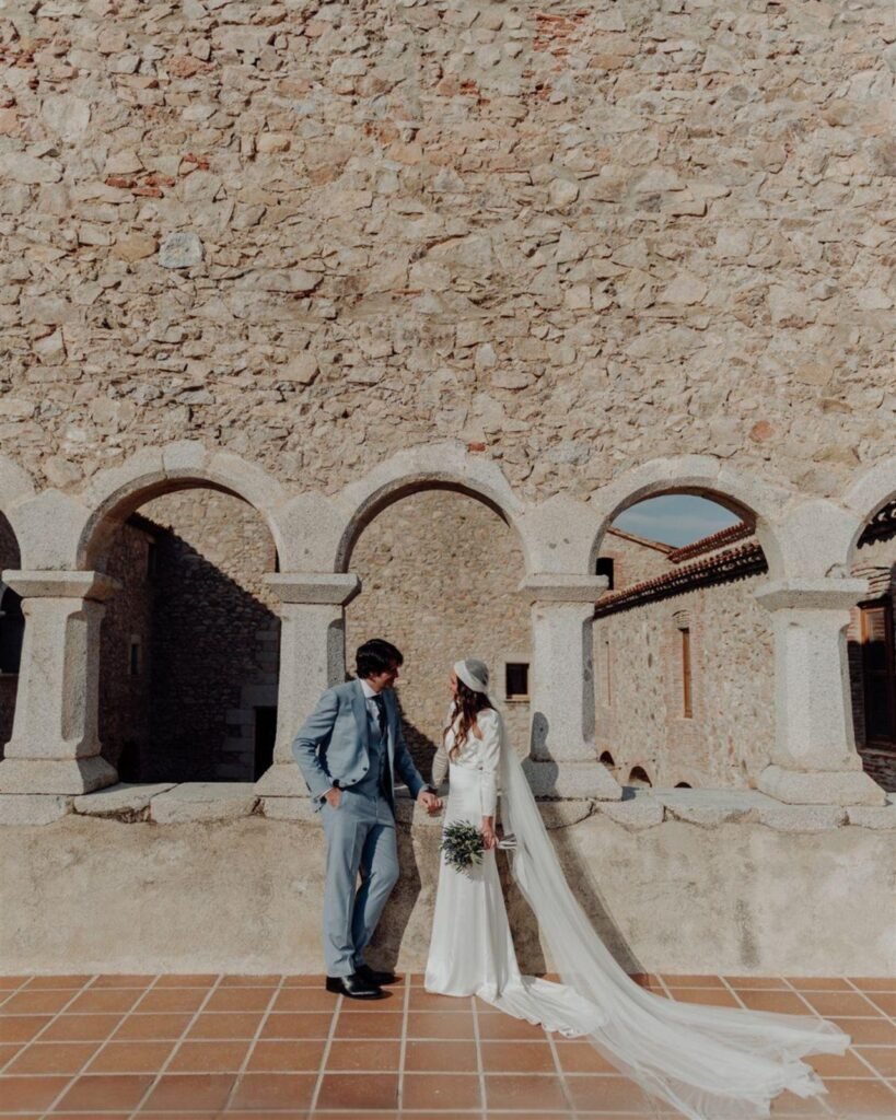Gemma y su pareja en el claustro de arcos del Monestir de Sant Salvi, vestido de satén de seda con velo largo de tul