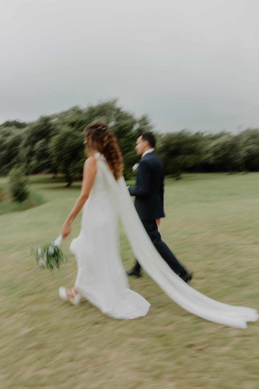 Mireia y su pareja caminando por un prado, con la capa de gasa plisada del vestido