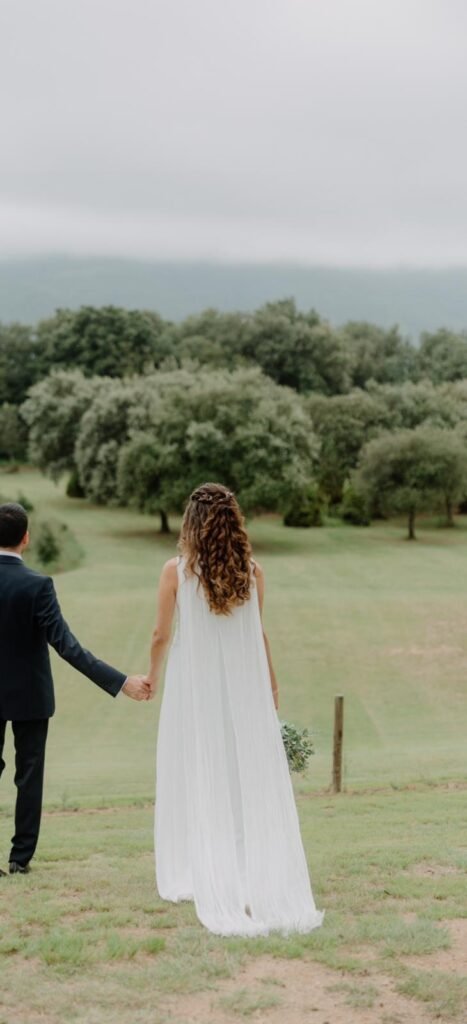 Mireia y su pareja de espaldas en un prado verde, con la capa de gasa plisada del vestido