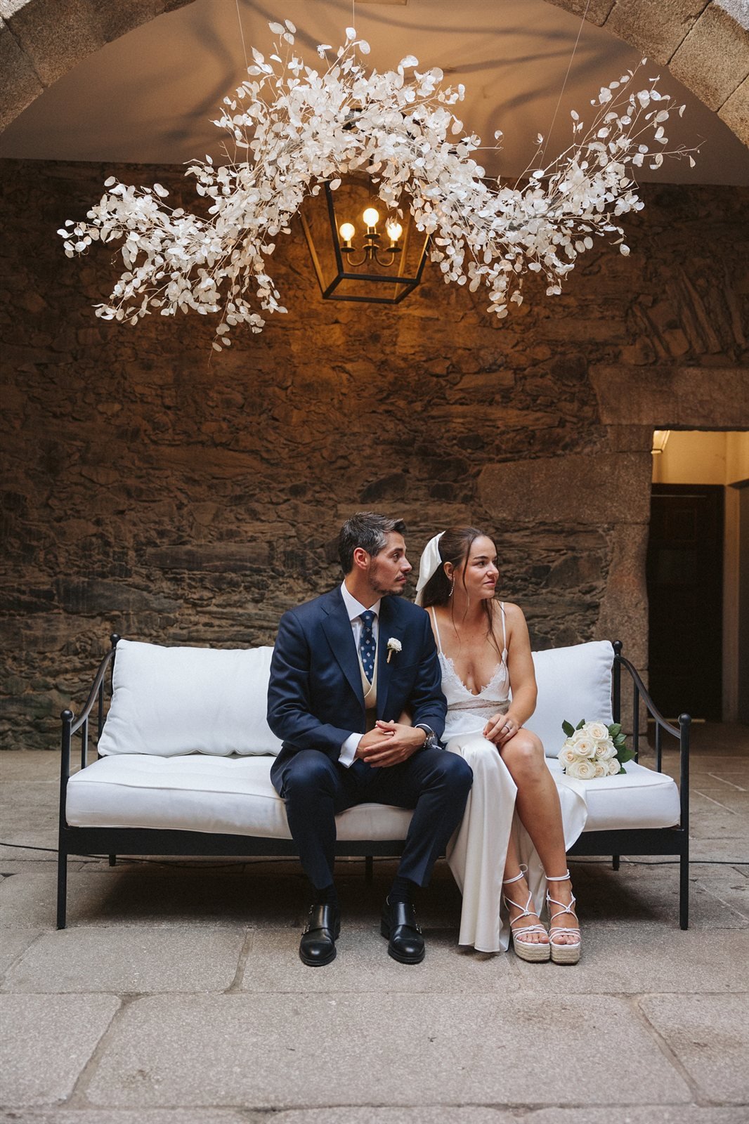 Nina e Iago sentados en un banco, boda en Galicia con interiores de piedra