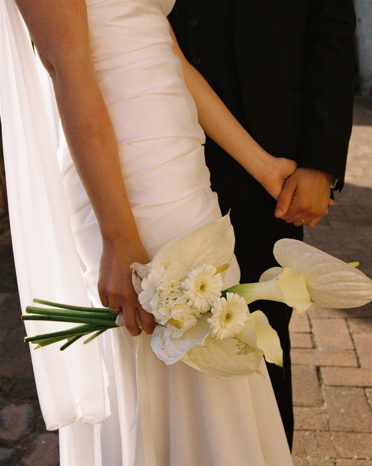 Detalle del cuerpo de mikado plisado a mano del vestido de Paula, con ramo blanco de anturios y calas