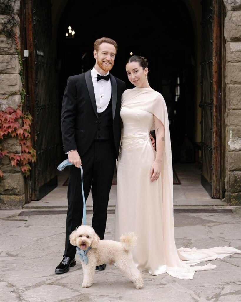 Paula Martos y su pareja con su perro a la entrada de La Baronia, vestido de crepé satén dorado con maxichal