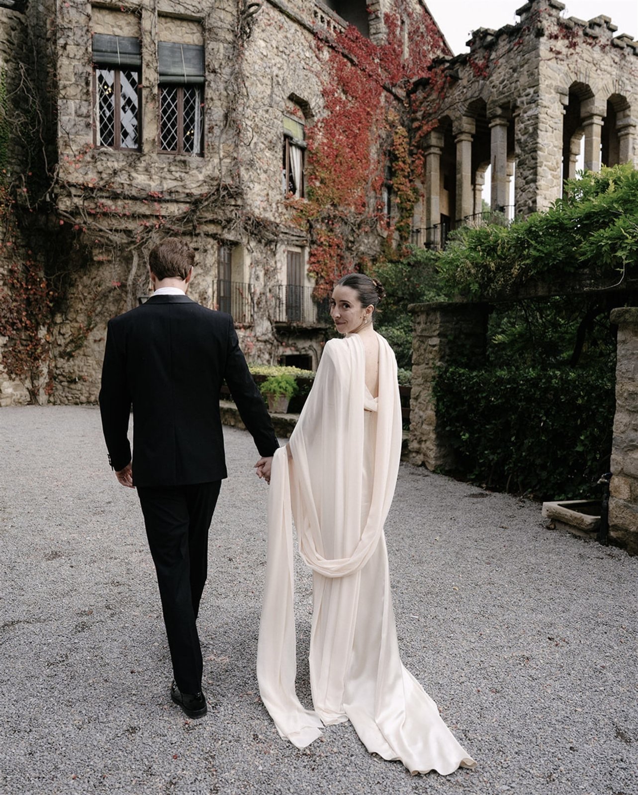 Paula y su pareja caminando hacia el edificio histórico de La Baronia con el maxichal del vestido, en otoño